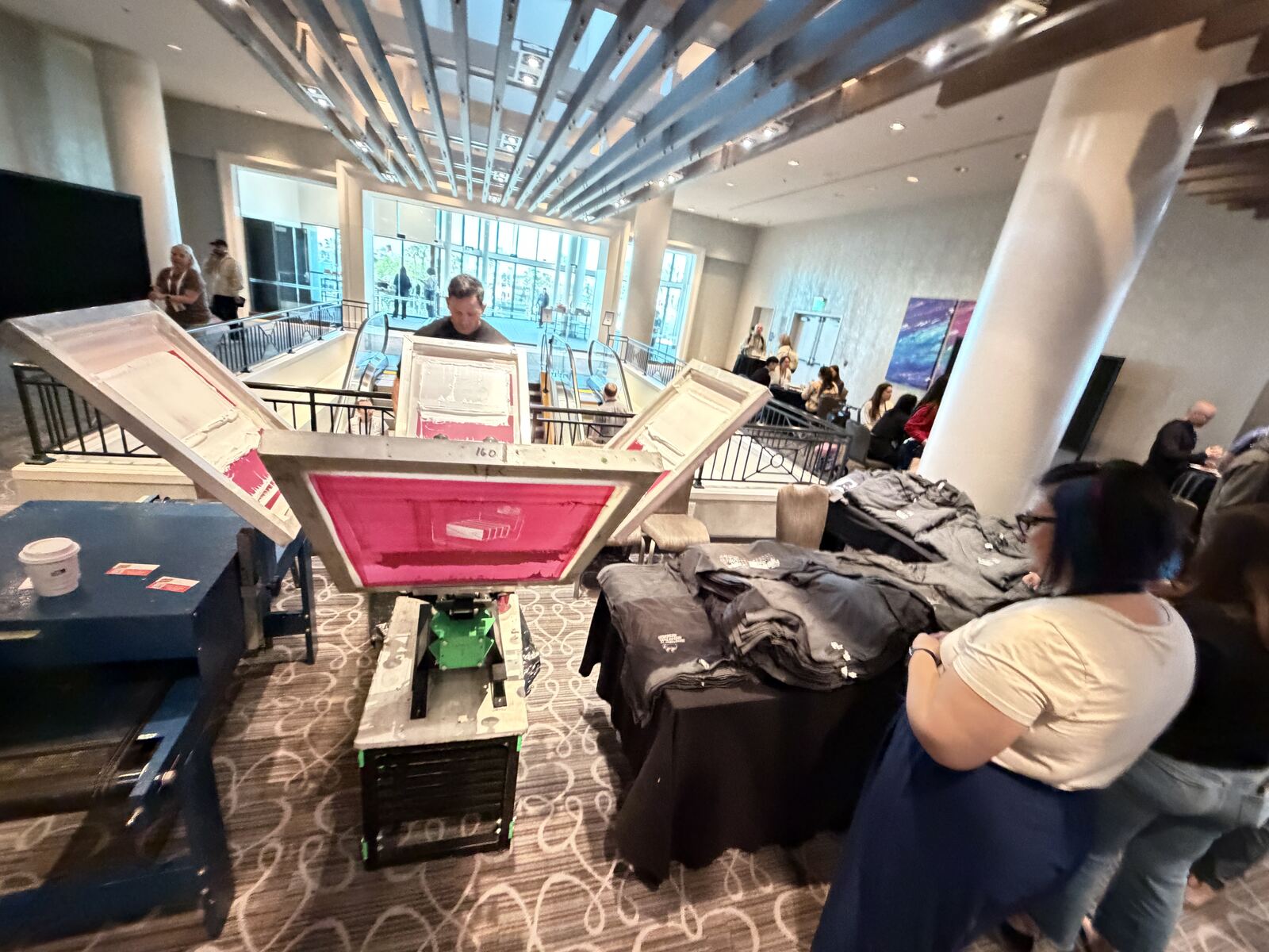 Large event or trade show space with multiple screen-printing equipment stations and decorated apparel samples